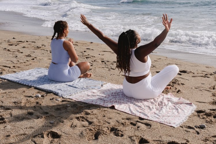 Two women do yoga together on the beach. Make new friendships in midlife by stepping out of your comfort zone.