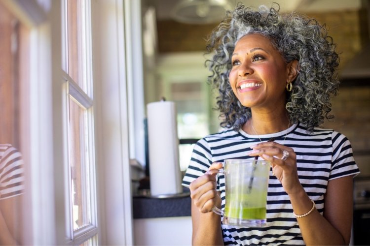 A woman drinks a smoothie and smiles while looking out the window.