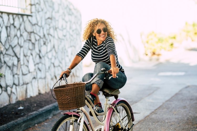 A woman full of joy embraces her midlife freedom by riding a pink and white bicycle.