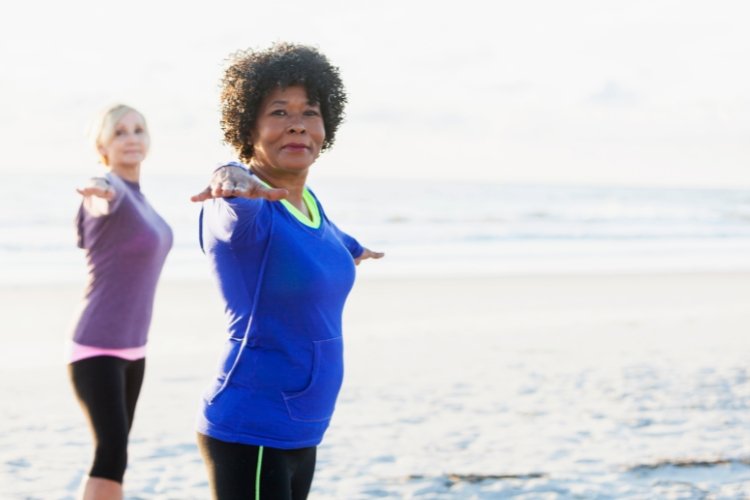 Two women do yoga on the beach.