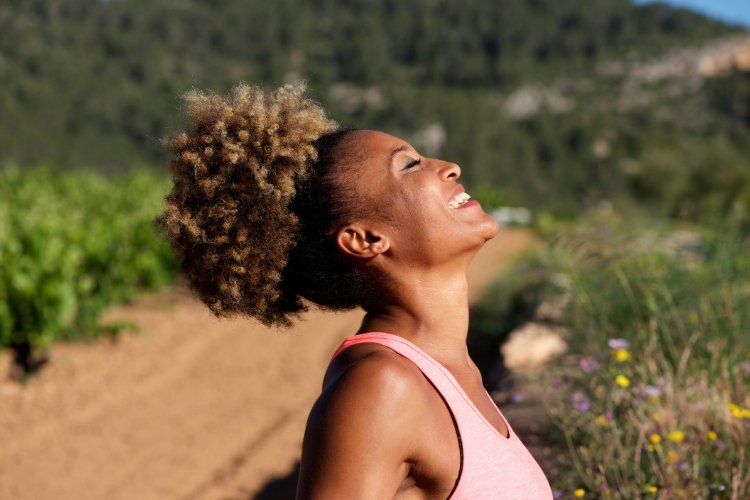 A woman is outside and smiling, eyes closed, at the sky.