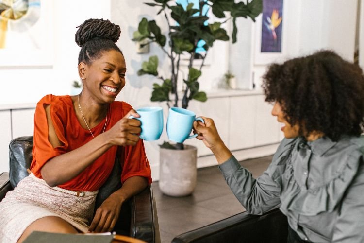 A smiling woman holds up a mug with a friend. Midlife Renaissance Collective connects middle-aged women.
