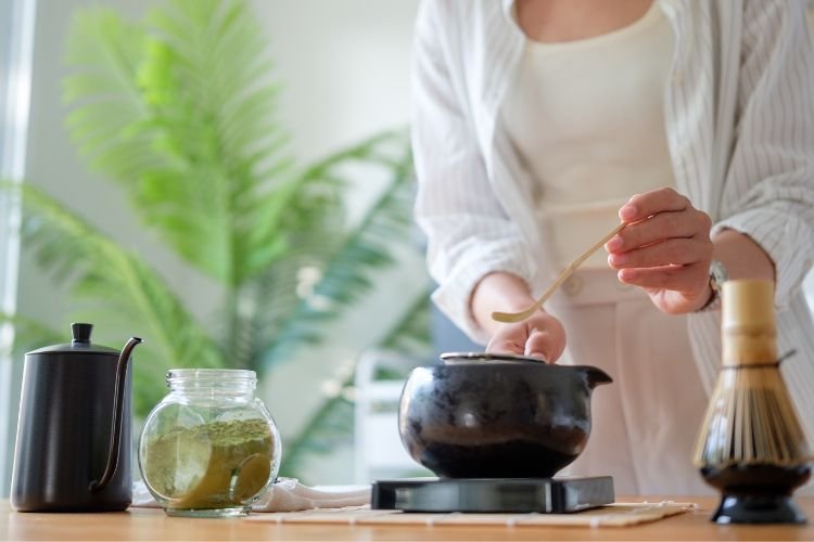 A woman carefully makes a cup of matcha tea as an example of a gratitude routine to create midlife happiness and resilience.