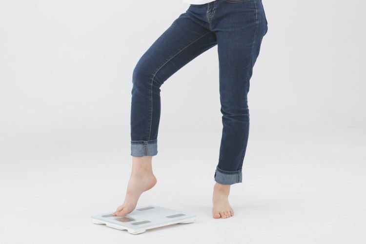 A woman in jeans stands on a scale. Weight is not an indicator of self-worth in midlife, or at any age.